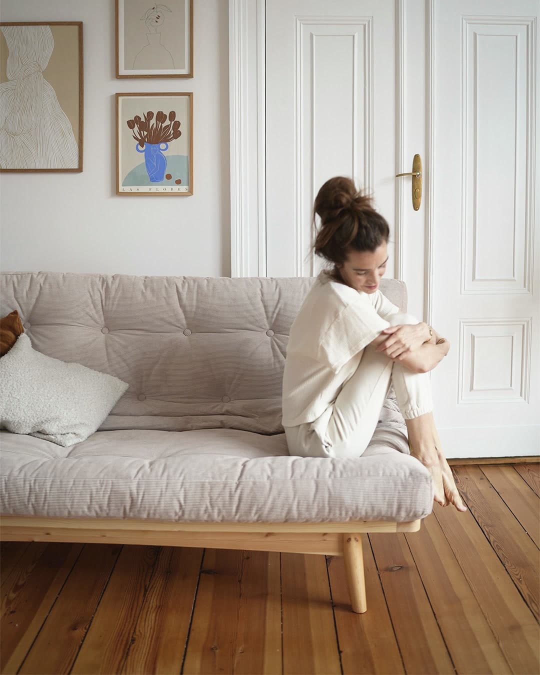 Mujer sentada abrazando sus rodillas en un futón en modo sofá, con base de madera sobre patas