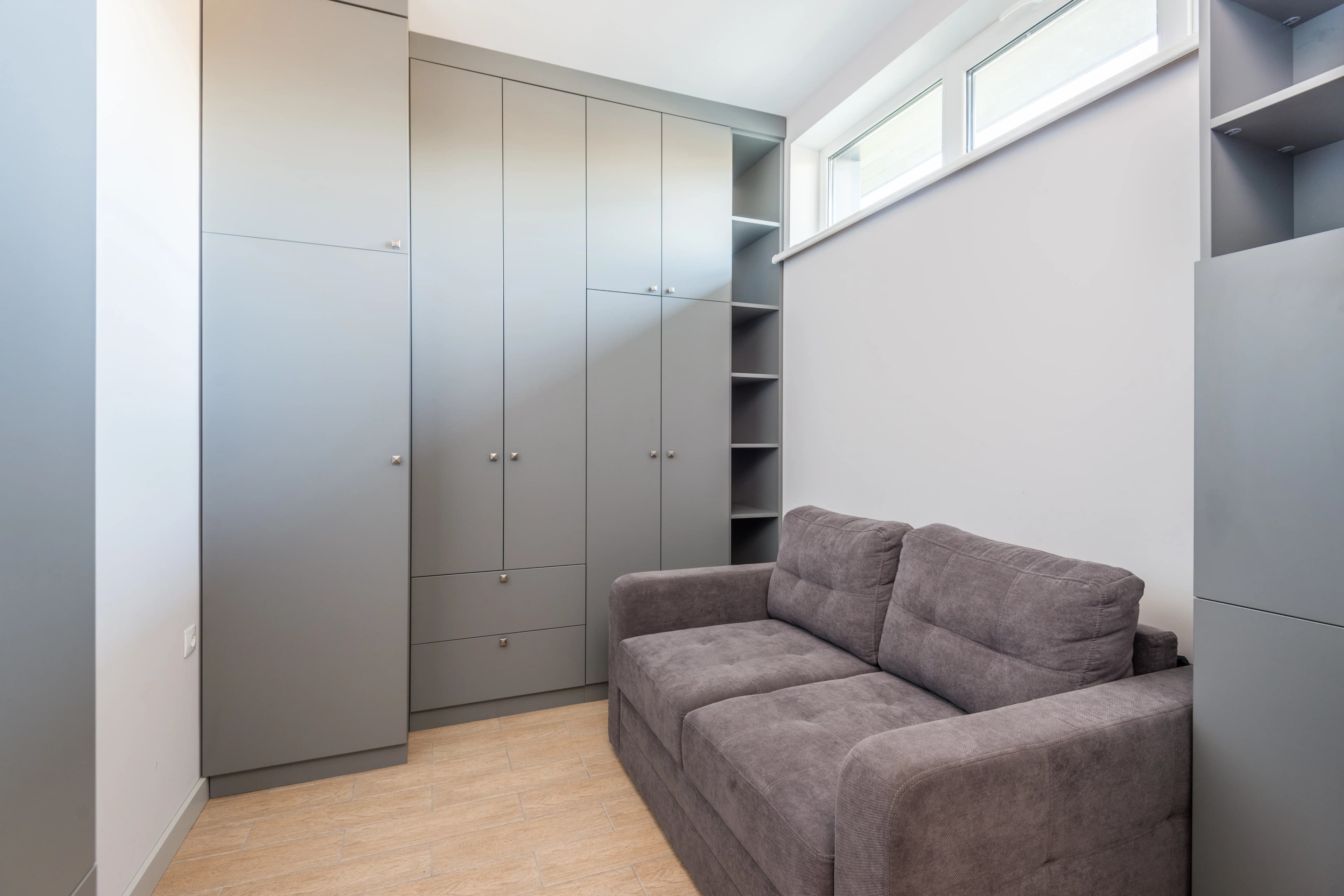 Sala pequeña con sofá claro de patas visibles, tapete y lámpara de piso junto a una ventana