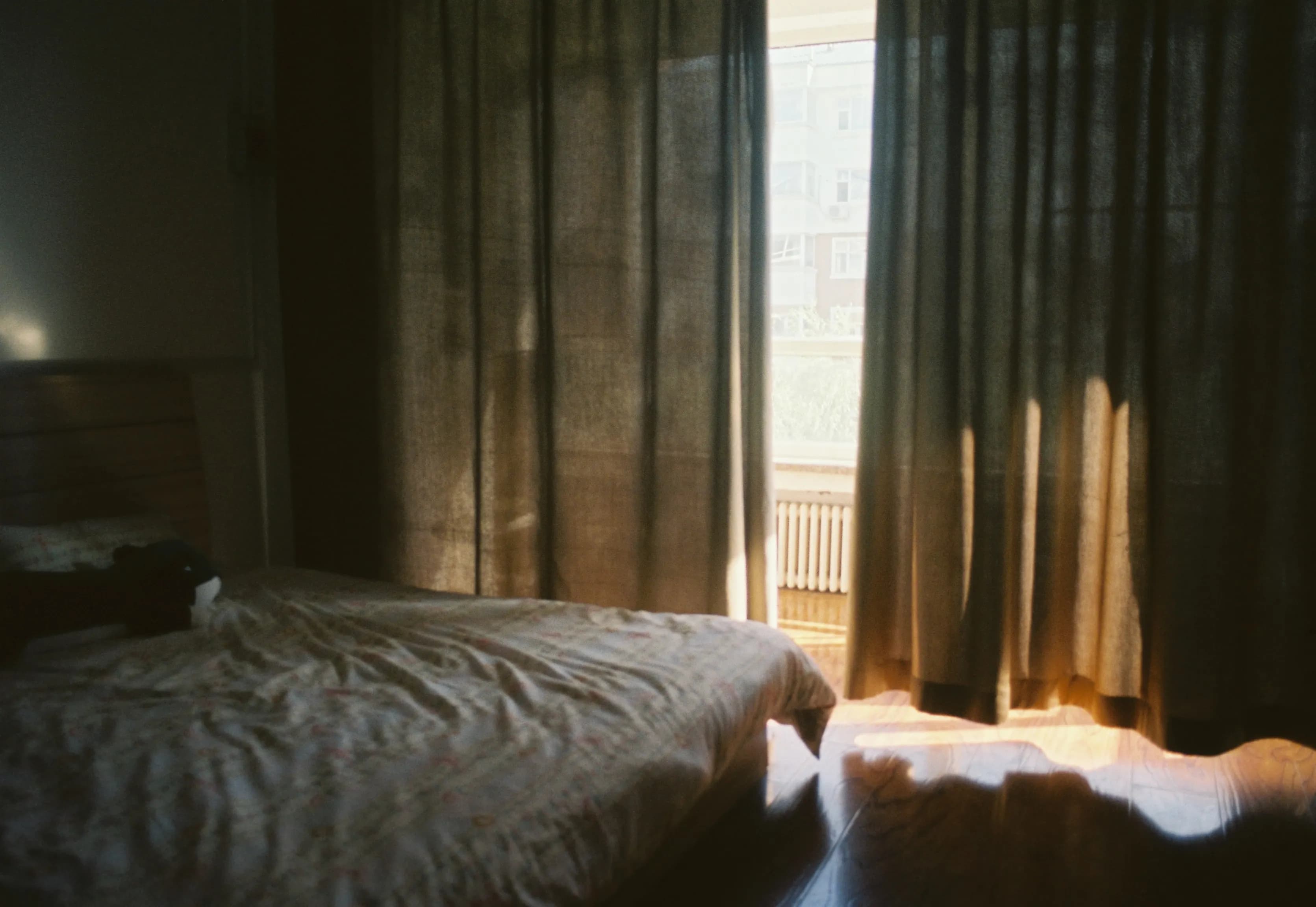 Recámara pequeña con cortinas entreabiertas y luz suave de la mañana entrando sobre la cama