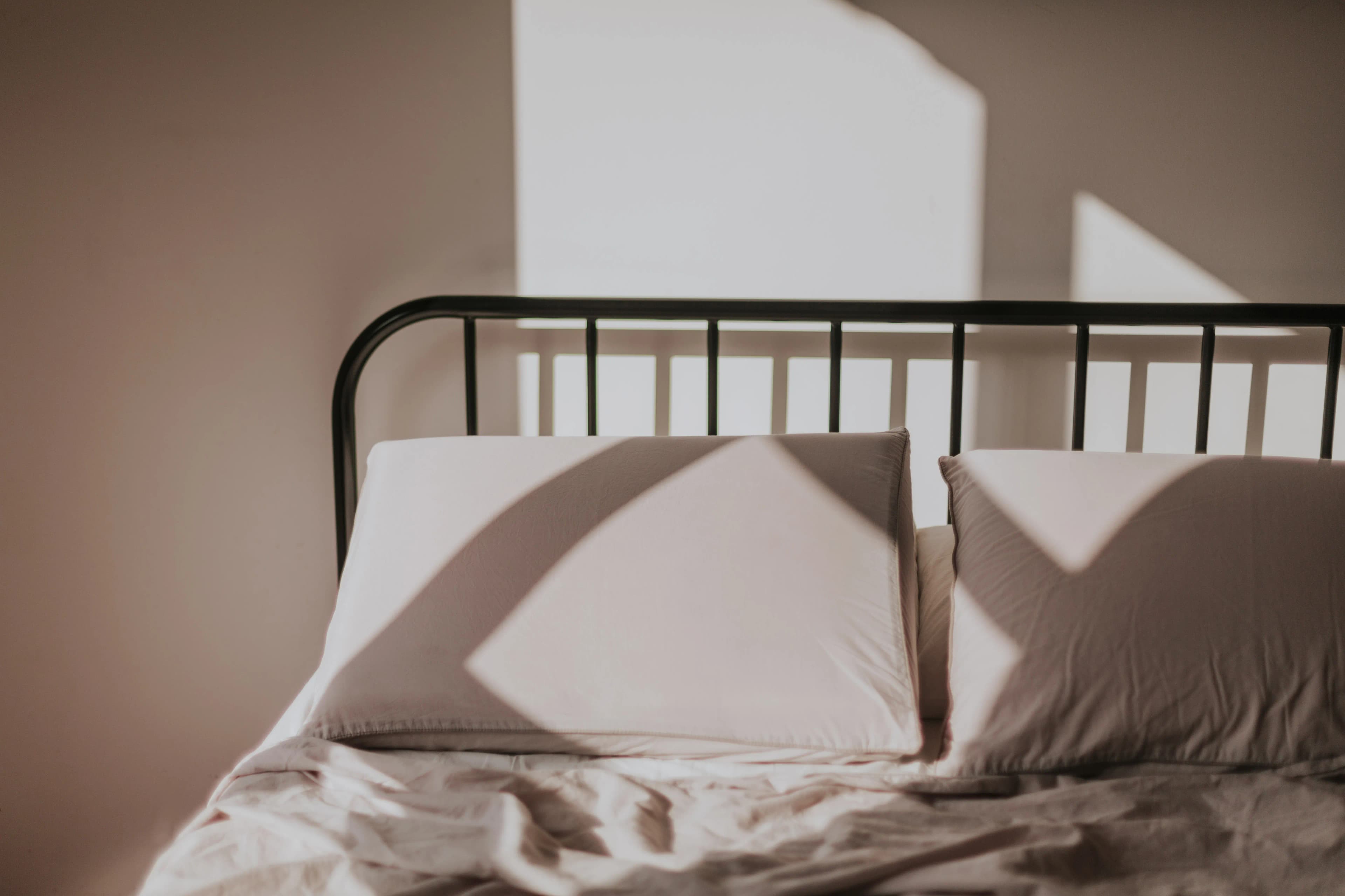 Cama con colchón y sábanas claras en una recámara pequeña iluminada por la luz de la mañana