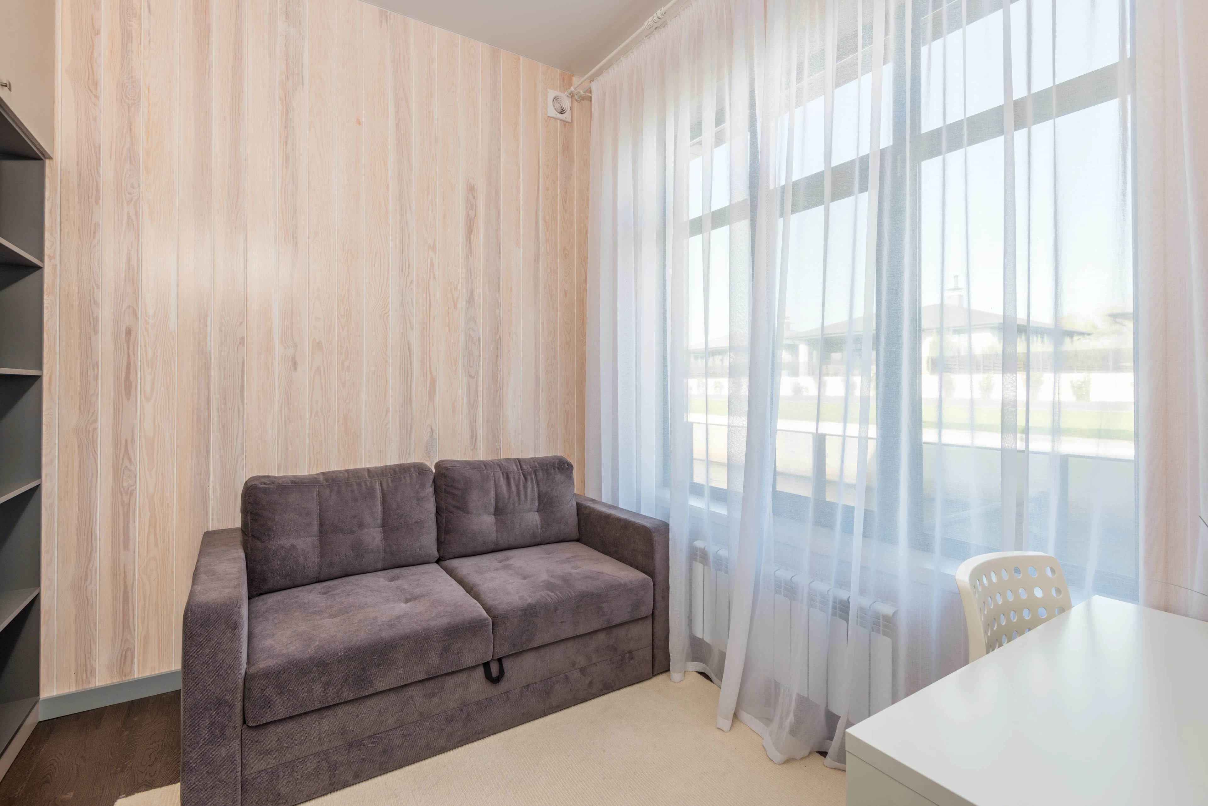 Sala pequeña con paredes claras, sofá neutro y cojines de color junto a una ventana